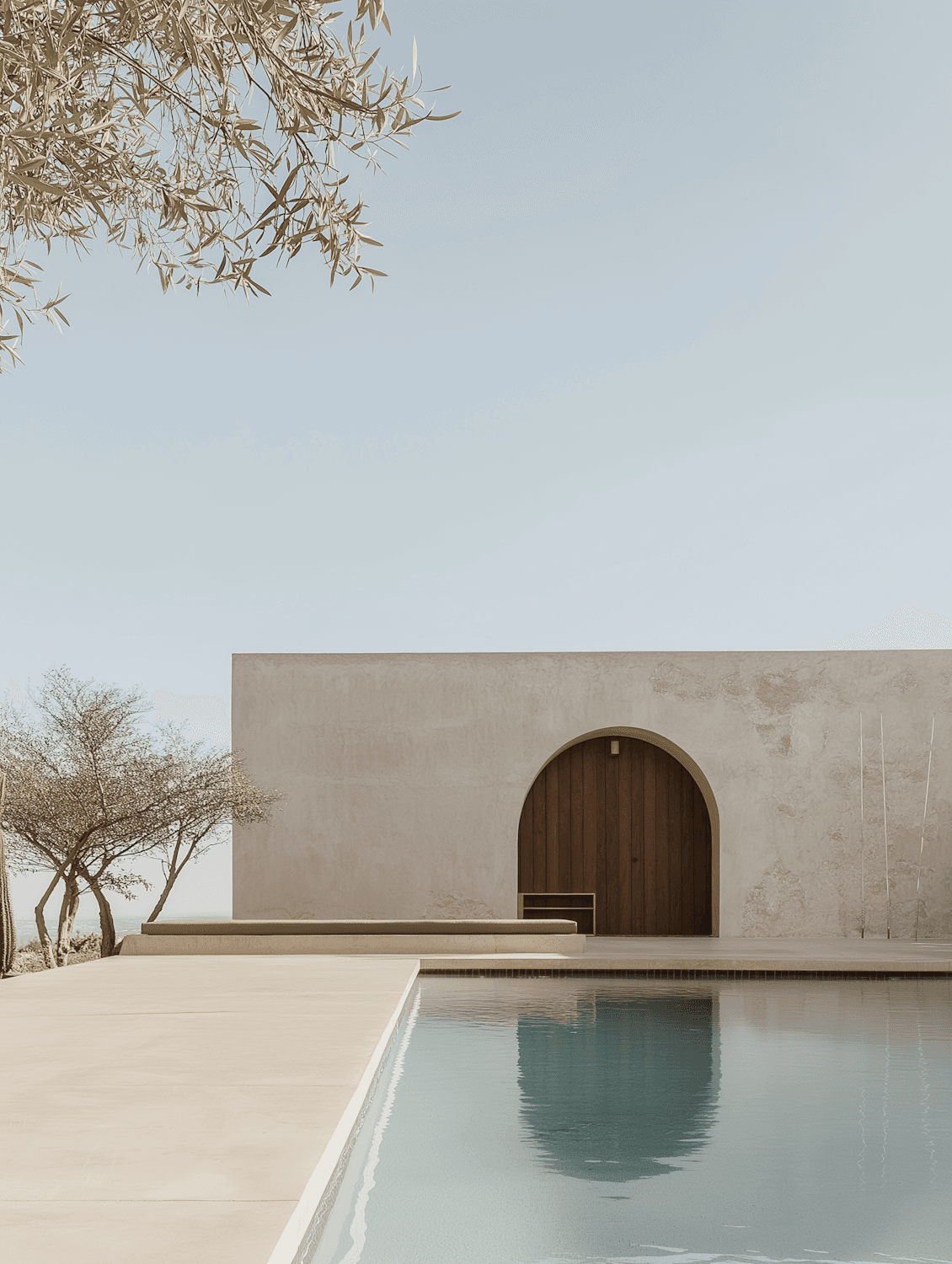 A lime-rendered wall with an arched timber door beside a still pool at Qila Retreat, under a clear desert sky.